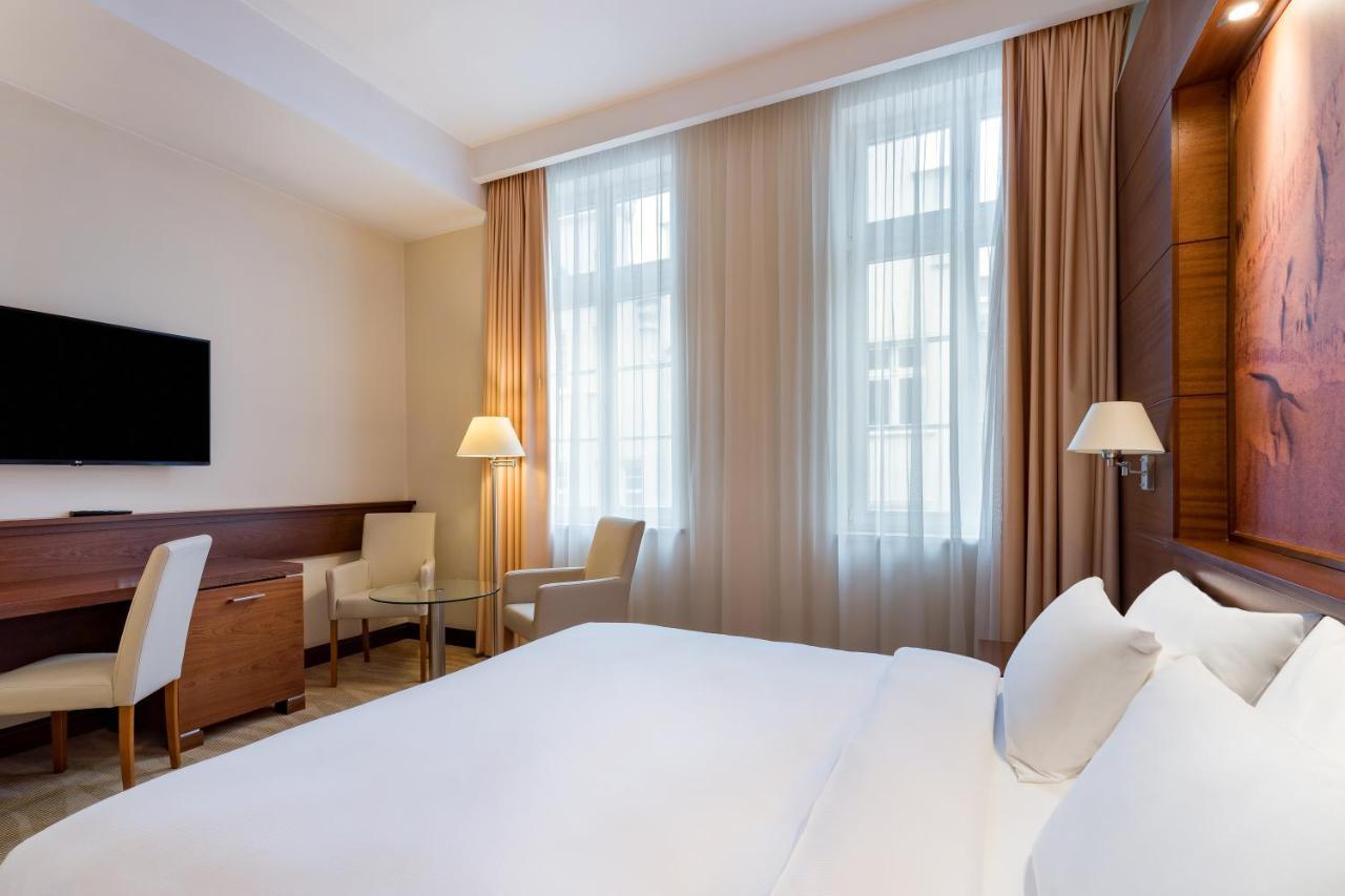 Radisson Blu Hotel, กดัญสก์ ภายนอก รูปภาพ The photo depicts a modern hotel room. It features a neatly made bed with white linens, flanked by two pillows. On the wall opposite the bed, there is a flat-screen television mounted. There are two windows with sheer curtains that allow natural ligh