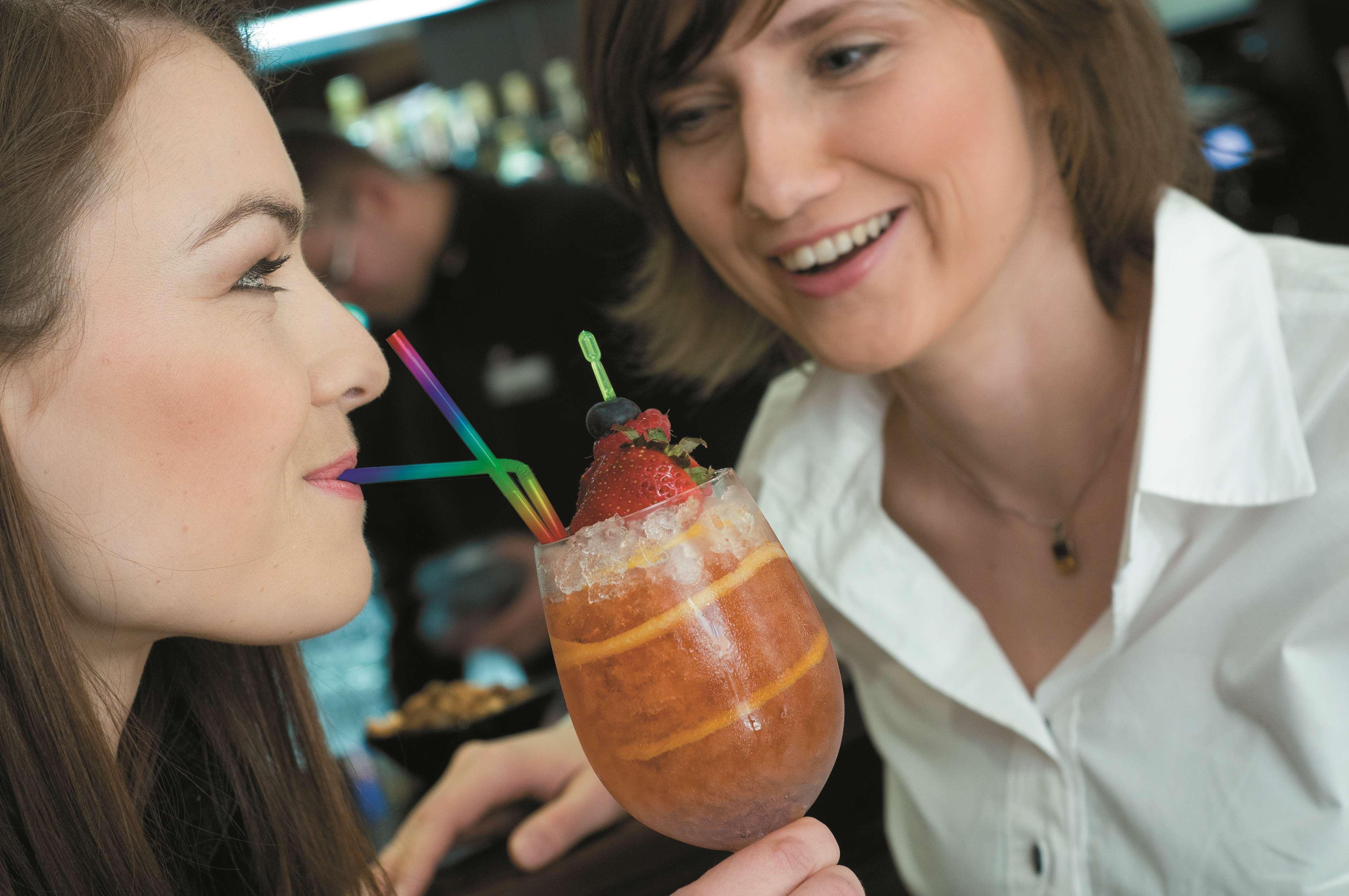 Radisson Blu Hotel, กดัญสก์ ภายนอก รูปภาพ The photo shows two women engaging with each other, smiling and enjoying a moment together. One woman is holding a colorful drink in a large glass adorned with ice, fruit, and multiple straws. The other woman looks on with a friendly expression, cont