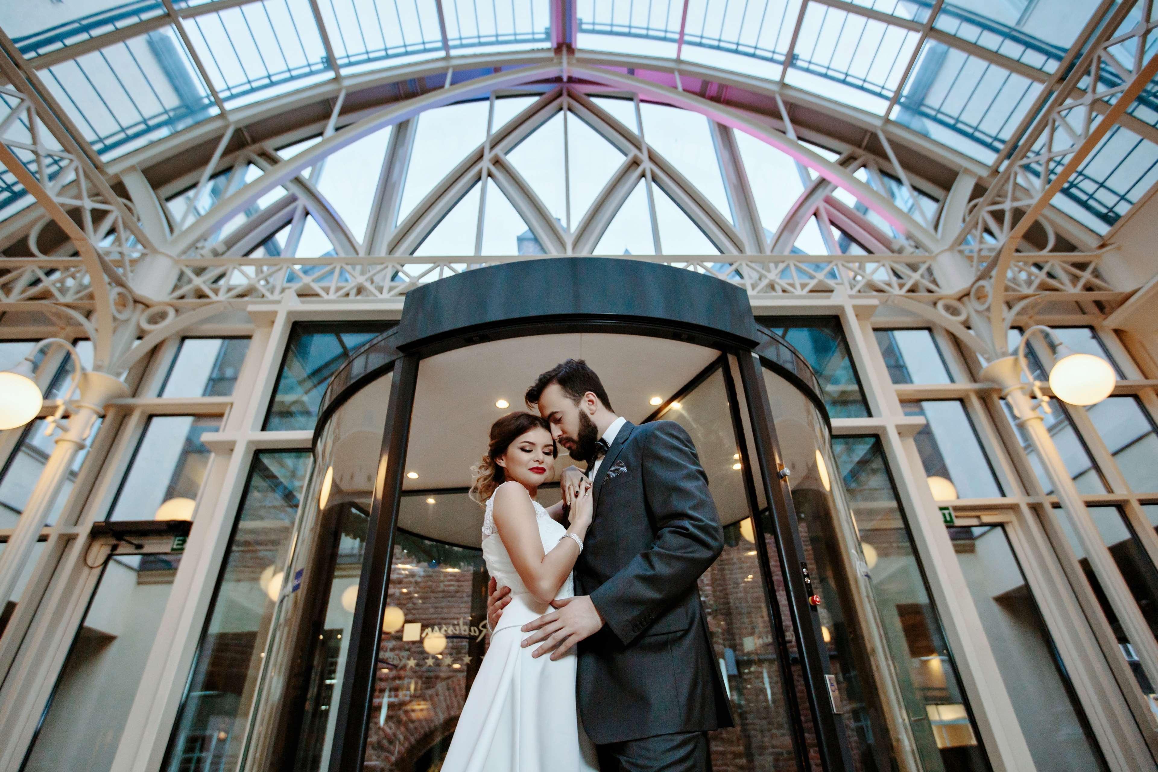 Radisson Blu Hotel, กดัญสก์ ภายนอก รูปภาพ The photo shows a romantic scene featuring a couple in formal attire, likely celebrating their wedding. They are positioned in front of a round glass door, which is partially open. The couple is standing close together, with their foreheads touching,