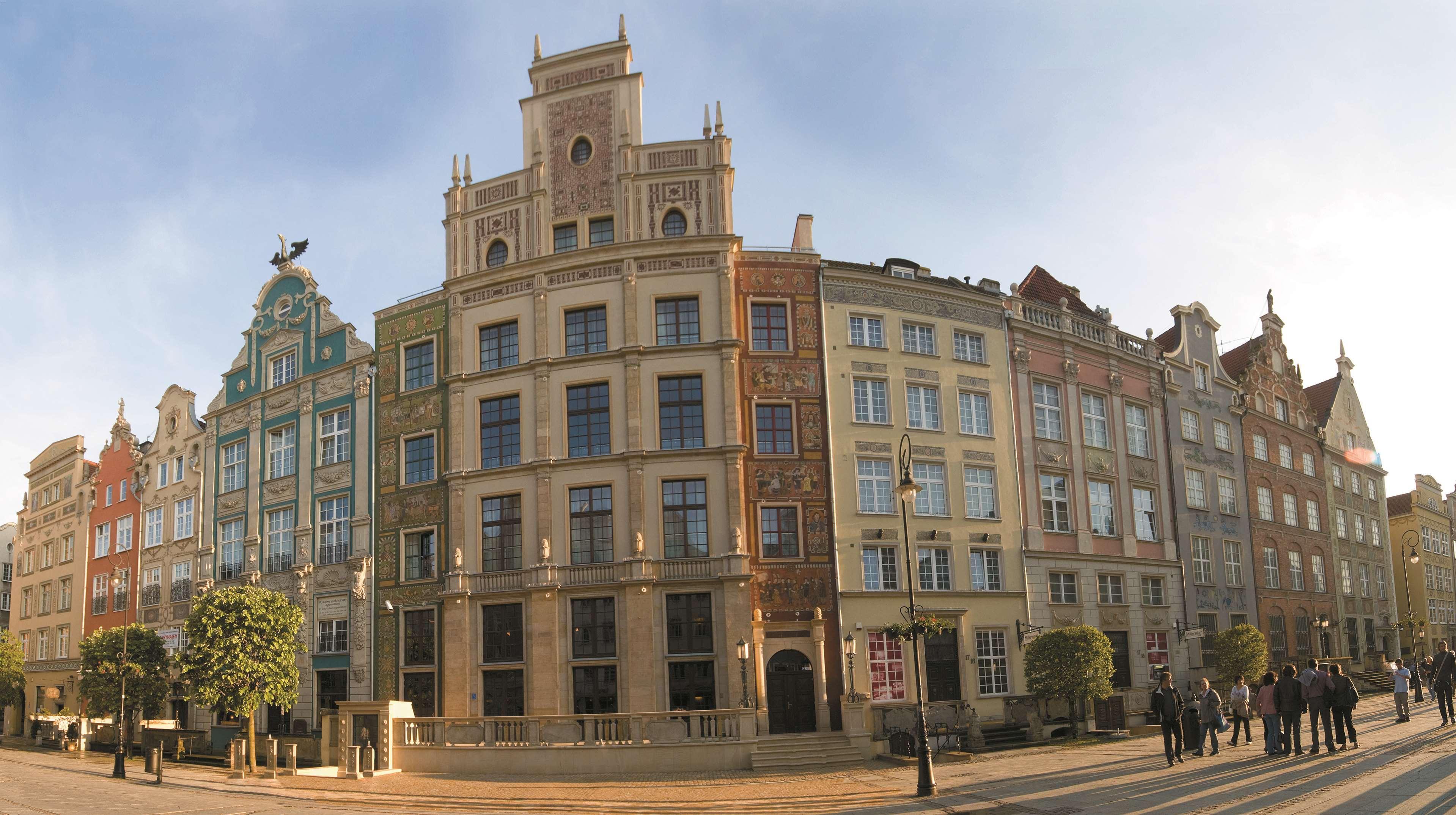 Radisson Blu Hotel, กดัญสก์ ภายนอก รูปภาพ The photo showcases a panoramic view of a row of historic buildings, likely in a European city. The architecture features a blend of styles, presenting a vibrant facade with multiple colors and decorative elements. Each building has distinct characte