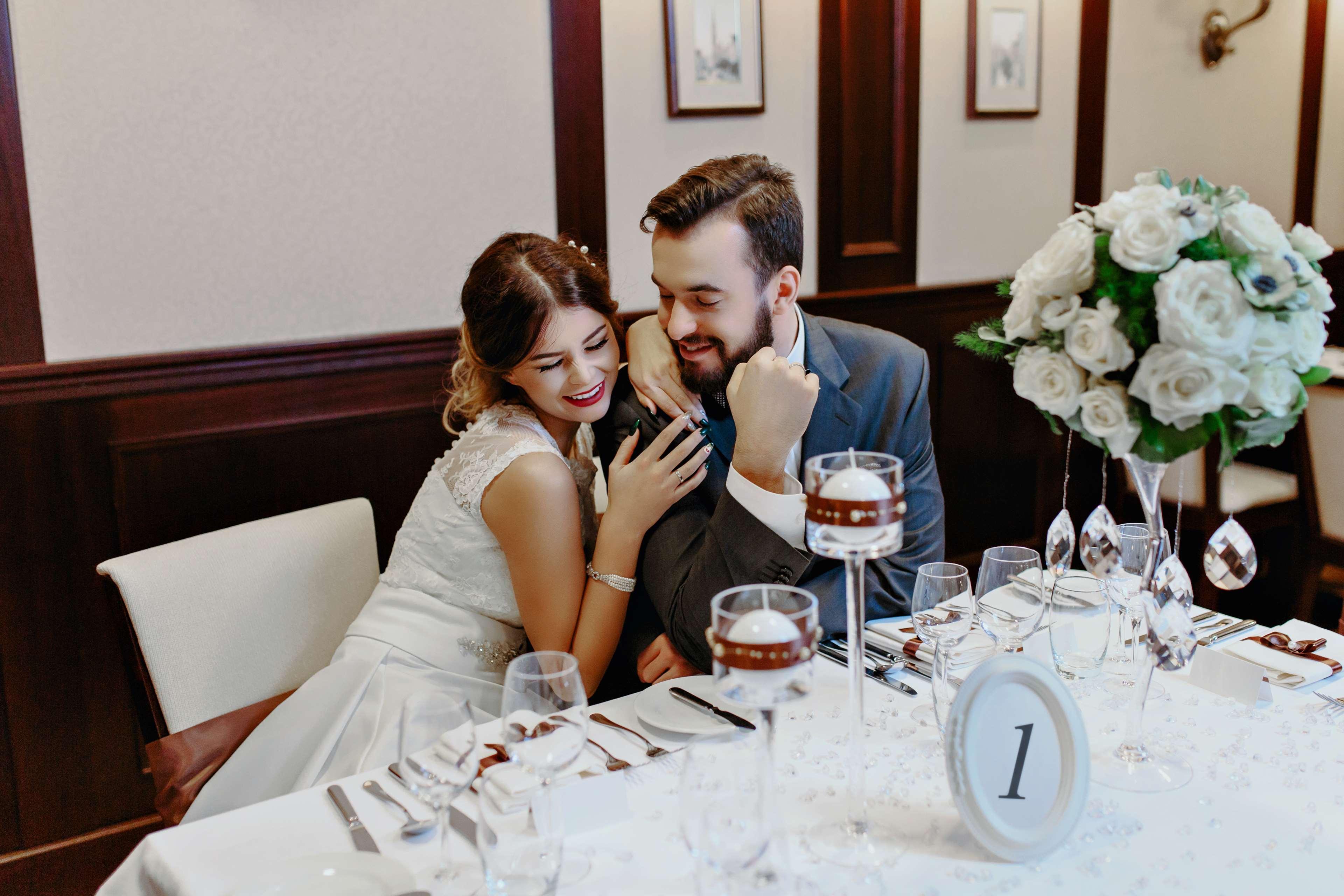 Radisson Blu Hotel, กดัญสก์ ภายนอก รูปภาพ The photo depicts a couple sitting at a beautifully arranged dining table. The woman, dressed in a white wedding gown, leans affectionately towards the man, who is wearing a gray suit. They appear to be enjoying a moment together, smiling and engagin