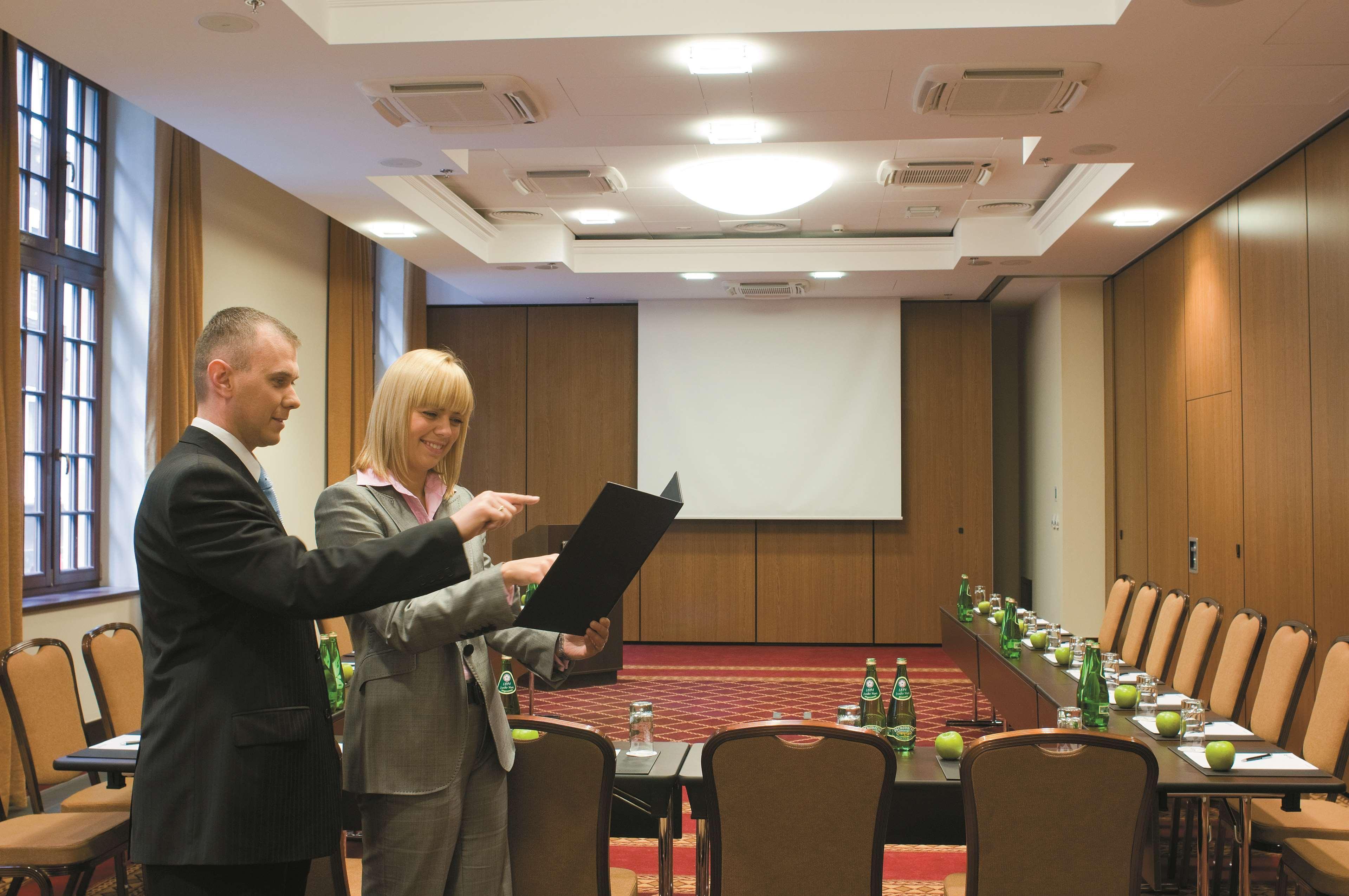 Radisson Blu Hotel, กดัญสก์ สิ่งอำนวยความสะดวก รูปภาพ The image shows a professional meeting room set up for a conference or presentation. There are two people in formal attire engaged in discussion; one is holding a document or folder while the other is pointing at it. The room features a large screen 