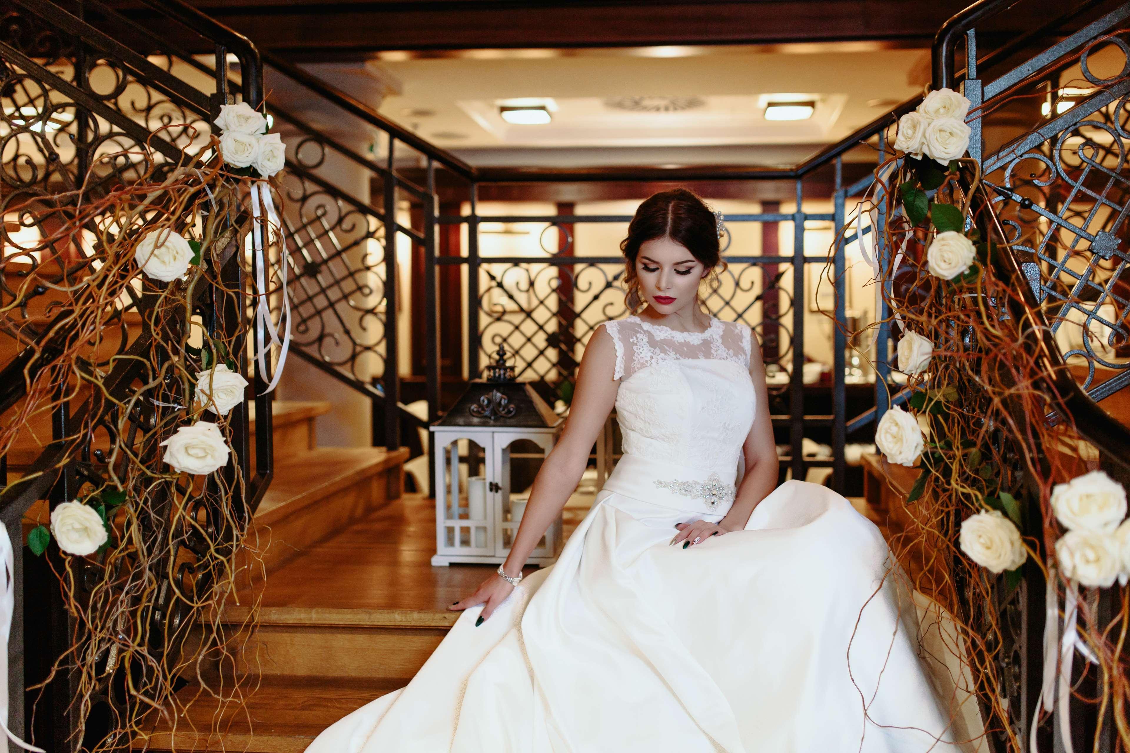 Radisson Blu Hotel, กดัญสก์ ภายนอก รูปภาพ The image shows a bride seated on a staircase in an elegant indoor setting. She is wearing a beautiful white wedding gown with intricate details, including a sheer neckline. The staircase is adorned with decorative elements, such as white roses and f