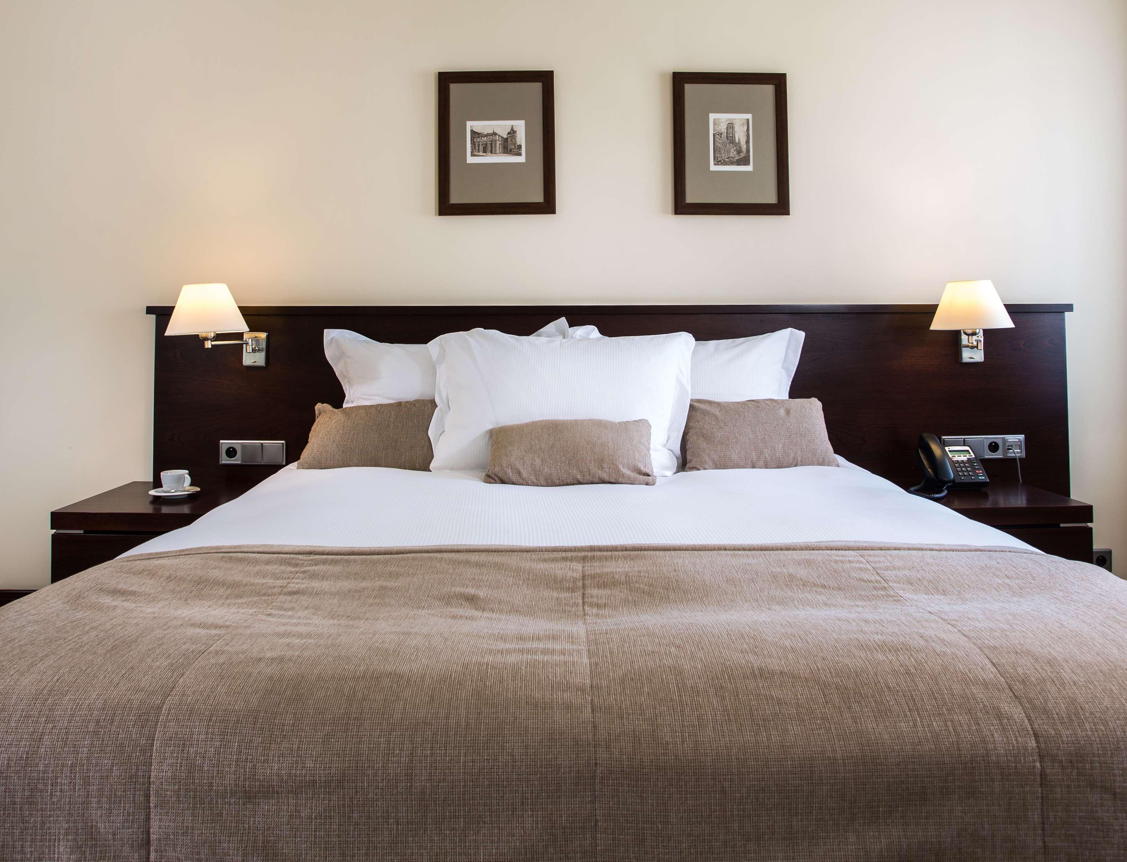 Radisson Blu Hotel, กดัญสก์ ภายนอก รูปภาพ The photo shows a well-decorated hotel room, focusing on a large bed with a dark wood headboard. The bed is adorned with several white pillows and a couple of beige cushions. There are two lamps on either side of the bed, providing soft lighting. Abo