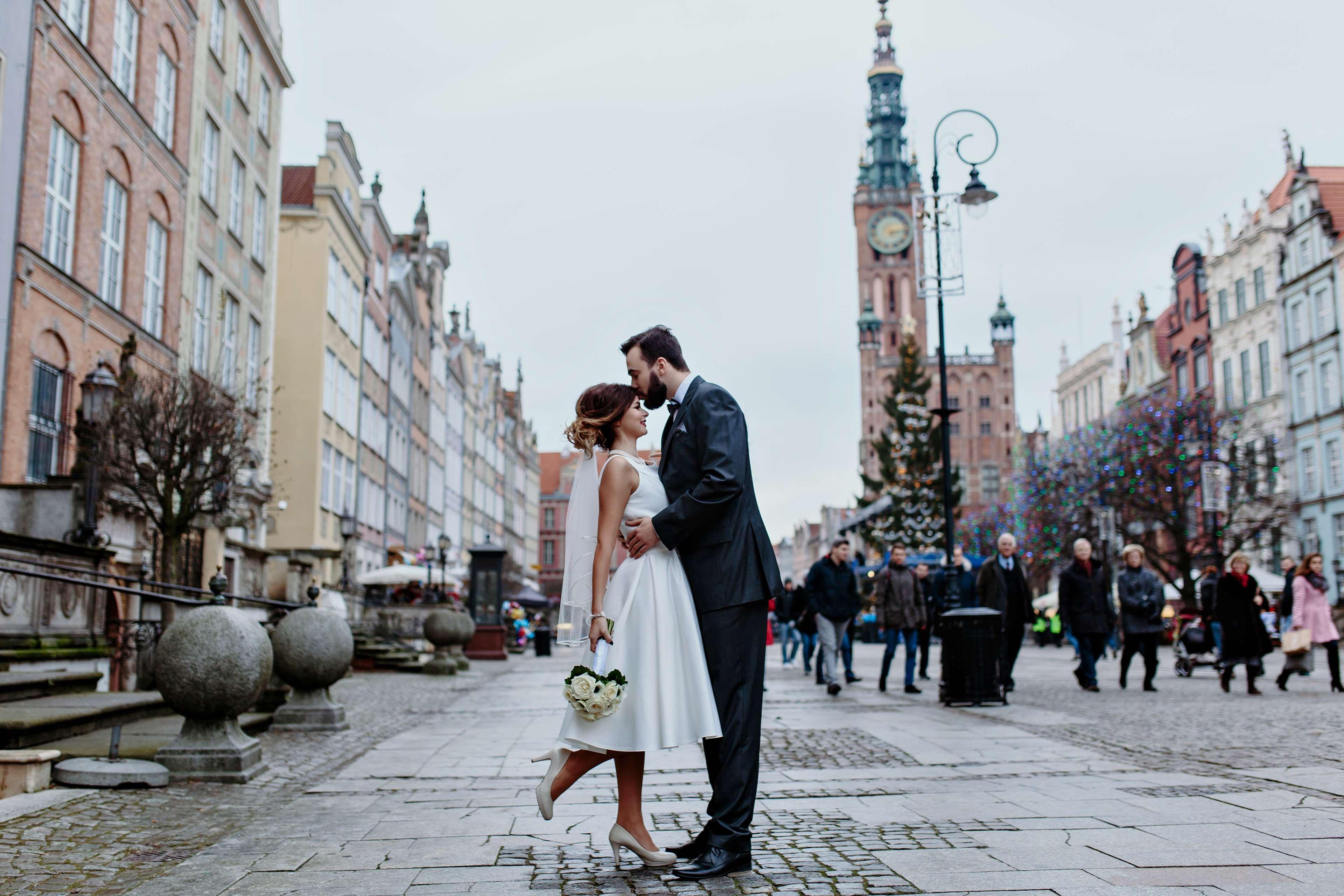 Radisson Blu Hotel, กดัญสก์ ภายนอก รูปภาพ The photo depicts a joyful moment between a couple in a romantic embrace on a lively street. The woman is wearing a white wedding dress, and the man is dressed in a smart suit. They appear to be celebrating their love, possibly on their wedding day. 