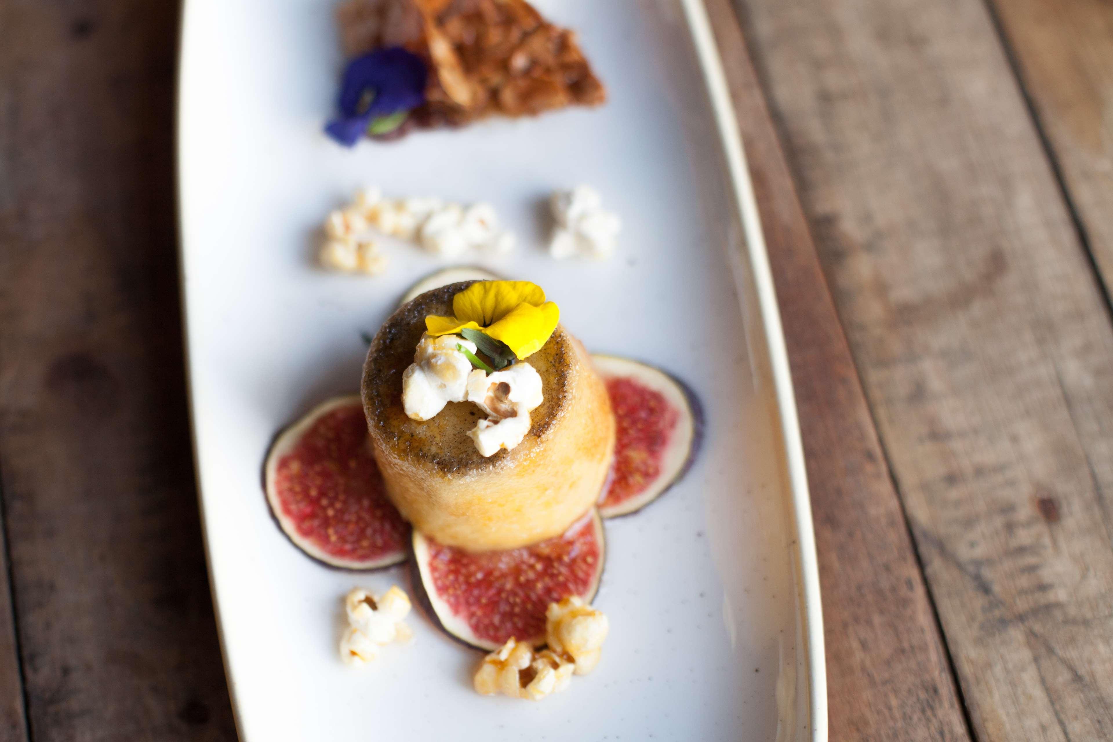 Radisson Blu Hotel, กดัญสก์ ภายนอก รูปภาพ The photo features an elegantly presented dessert on a white plate. In the center, there is a small dome-shaped cake topped with a yellow flower and popcorn. Surrounding it are slices of fig and scattered popcorn. To the side, there is a piece of a c
