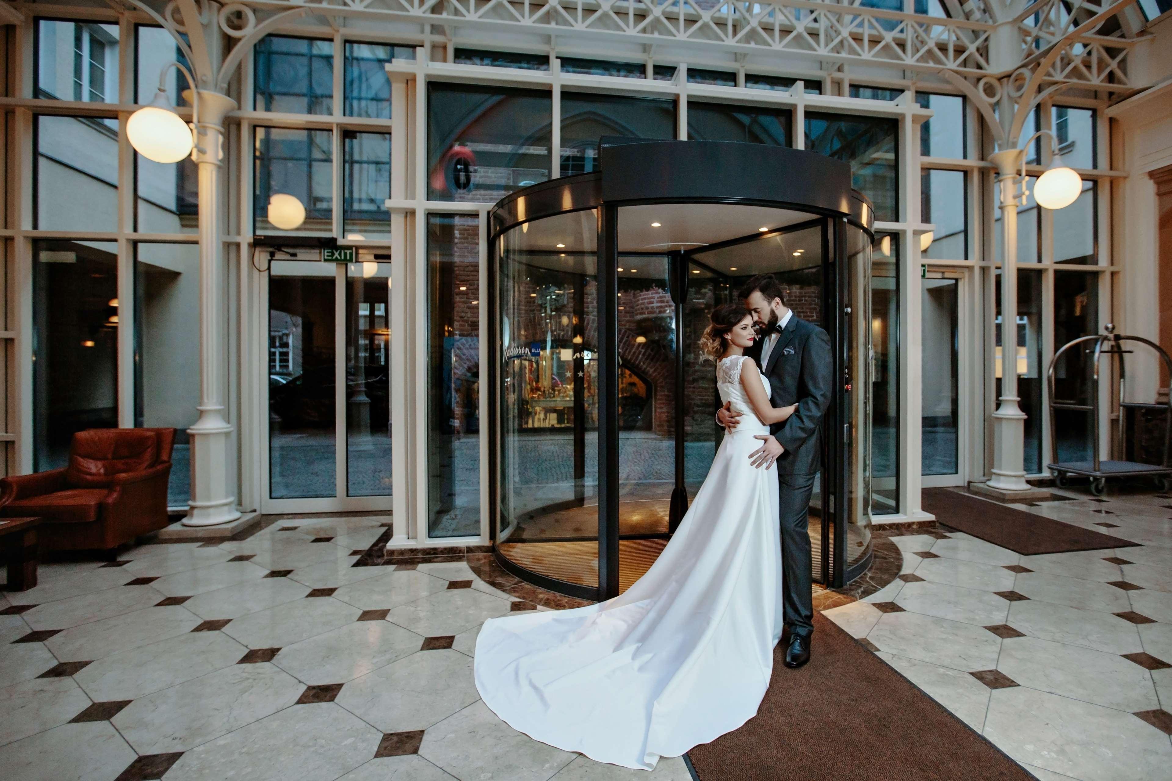 Radisson Blu Hotel, กดัญสก์ ภายนอก รูปภาพ The photo shows a couple in formal attire standing outside a building, likely a hotel or venue. They appear to be newlyweds, with the woman in a beautiful white wedding gown and the man in a suit. They embrace each other tenderly in front of a glass 
