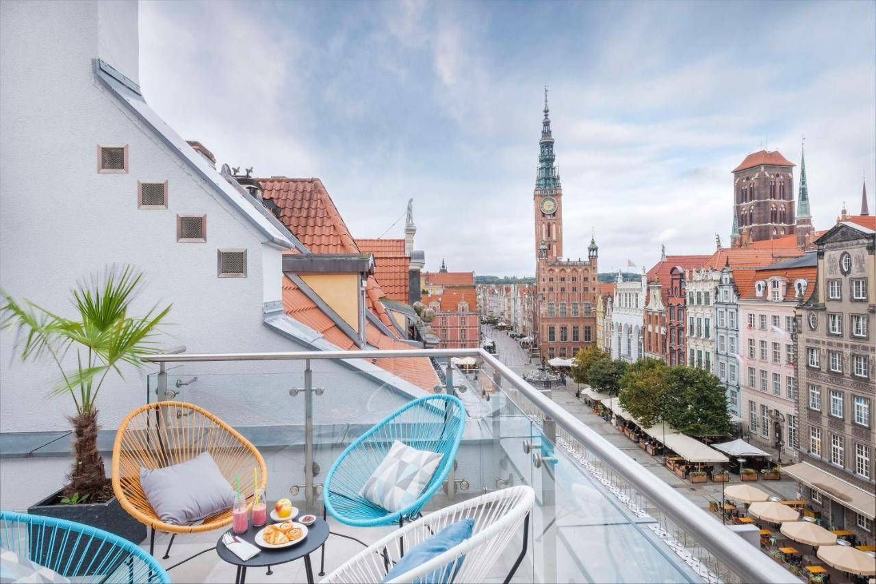 Radisson Blu Hotel, กดัญสก์ ภายนอก รูปภาพ The photo shows a stylish balcony overlooking a scenic urban landscape. There are two colorful chairs in blue and white, positioned around a small table. On the table, there are desserts and drinks, suggesting a cozy spot for relaxation. In the backg