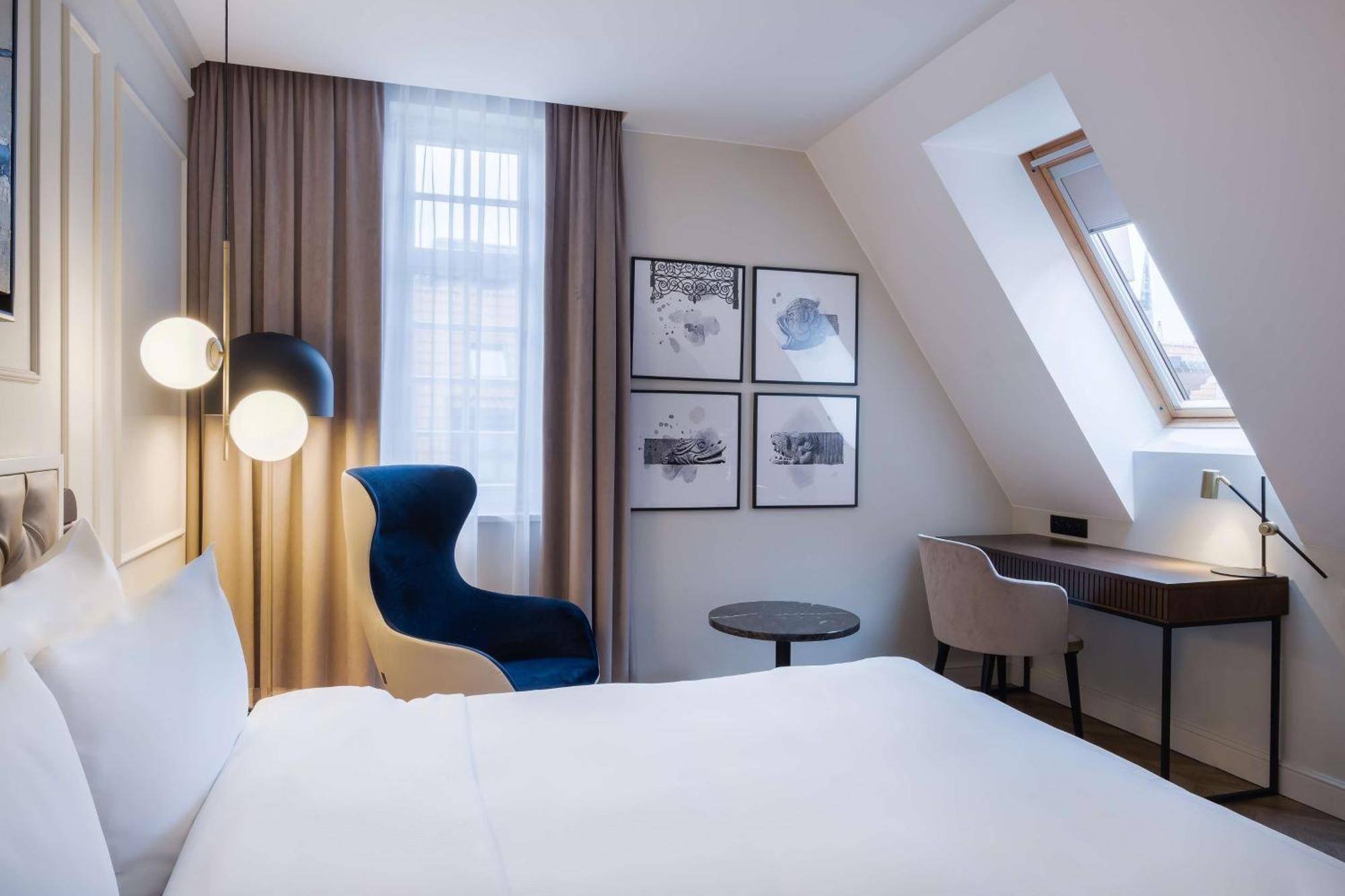 Radisson Blu Hotel, กดัญสก์ ภายนอก รูปภาพ The photo shows a cozy hotel room featuring a modern design. The room has a double bed with a white duvet, and a large window with sheer curtains that allows natural light to filter in. On the wall opposite the bed, there are several framed artworks.