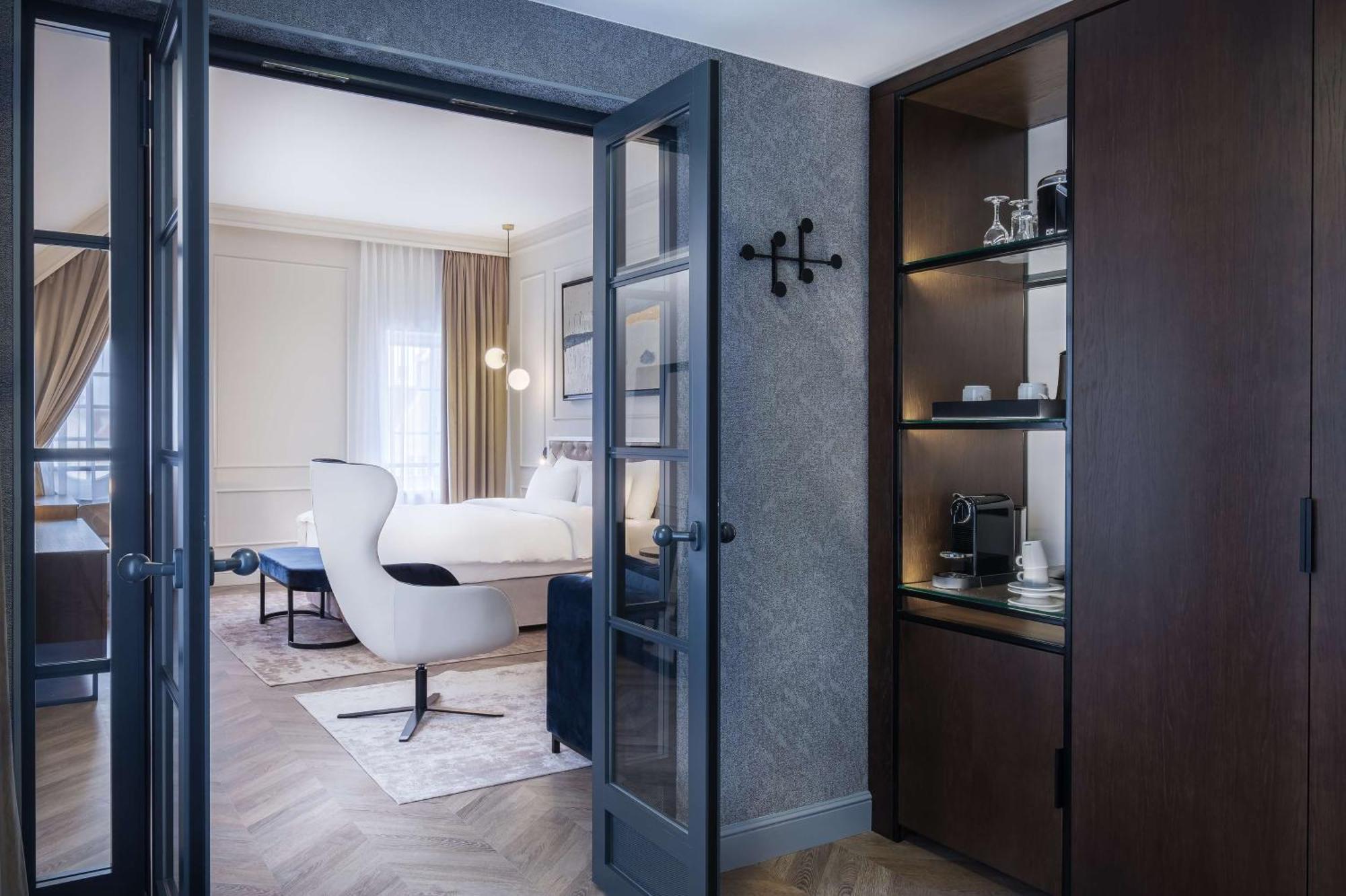 Radisson Blu Hotel, กดัญสก์ ภายนอก รูปภาพ The photo shows a luxuriously designed hotel room viewed from an entrance. In the foreground, there is a doorway with dark double doors leading into the main area. To the right, there is a wooden cabinet with shelves displaying some items, including 